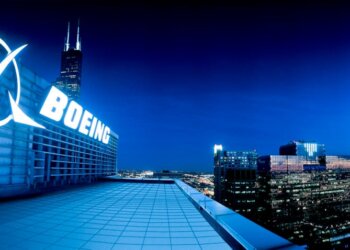 Boeing logo illuminated on a building rooftop at night with city skyline in the background.
