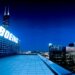 Boeing logo illuminated on a building rooftop at night with city skyline in the background.