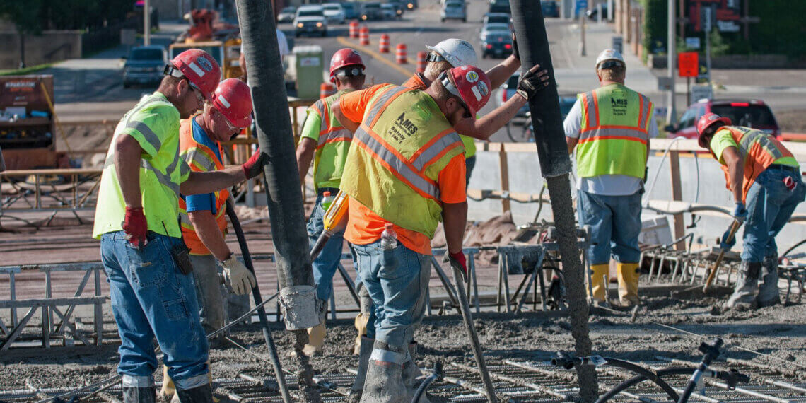 Group of construction workers in safety vests pouring concrete at a construction site.