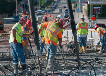 Group of construction workers in safety vests pouring concrete at a construction site.