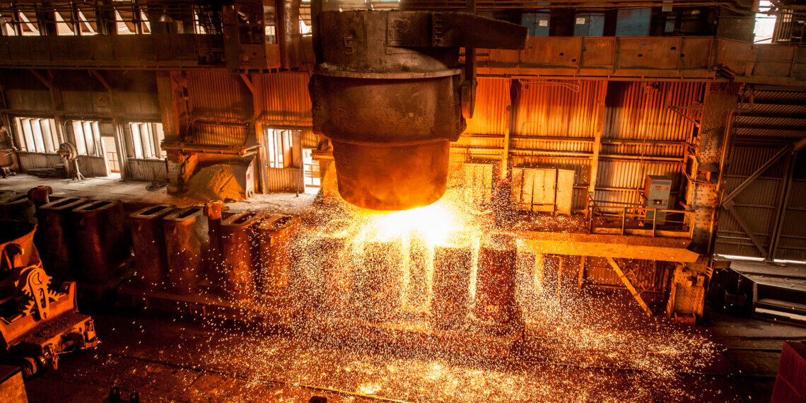 Molten metal being poured from a ladle in an industrial foundry, with sparks flying in the air.