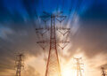 Silhouetted high voltage power lines and towers against a sunset sky with clouds.