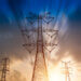 Silhouetted high voltage power lines and towers against a sunset sky with clouds.