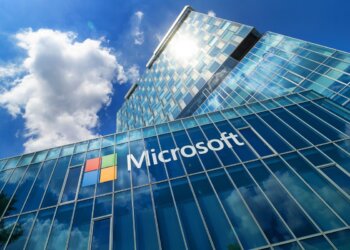 Microsoft office building with a glass facade reflecting the sky and clouds.