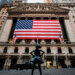 New York Stock Exchange building featuring a large American flag and a bronze statue of a girl in front.