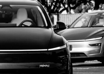 A black electric car and a silver electric car parked next to each other in a monochrome setting.