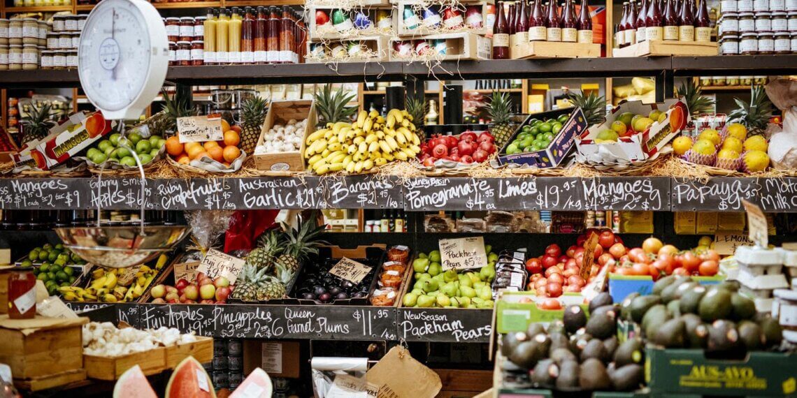 Variety of fruits and vegetables displayed on shelves in a grocery store.