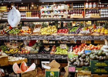 Variety of fruits and vegetables displayed on shelves in a grocery store.