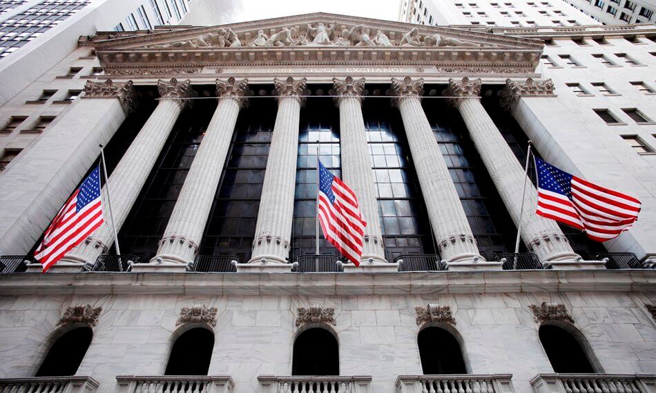 Facade of the New York Stock Exchange building with American flags and columns.