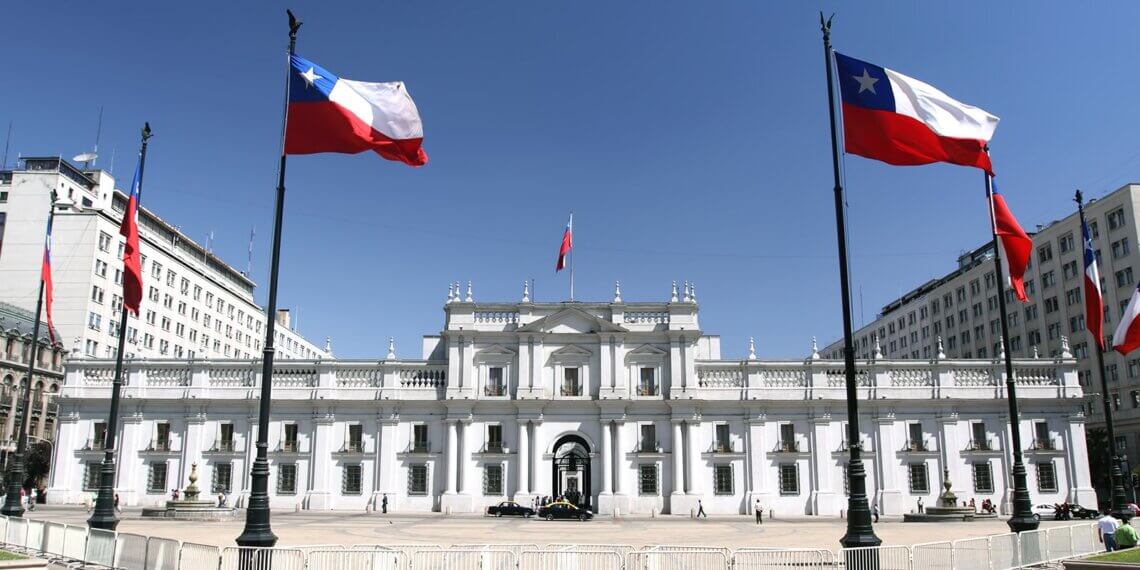 La Moneda Palace in Santiago, Chile, with Chilean flags displayed in front.
