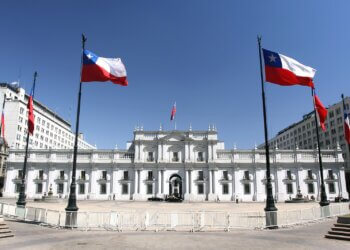 La Moneda Palace in Santiago, Chile, with Chilean flags displayed in front.