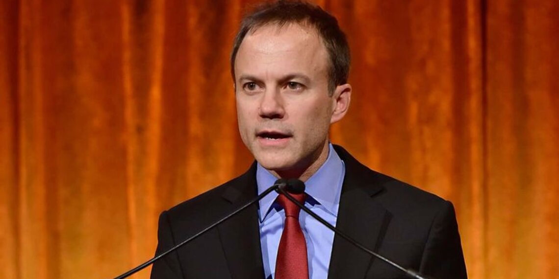 A man in a suit speaking at a podium with a microphone during an event.