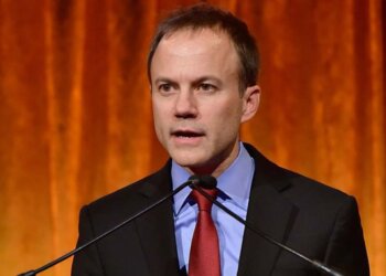 A man in a suit speaking at a podium with a microphone during an event.