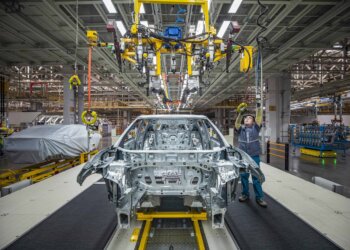 A worker inspecting a car chassis on an assembly line in a manufacturing facility.