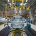 A worker inspecting a car chassis on an assembly line in a manufacturing facility.