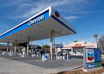 Chevron gas station canopy with fuel pumps and signage in a clear blue sky.
