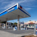 Chevron gas station canopy with fuel pumps and signage in a clear blue sky.