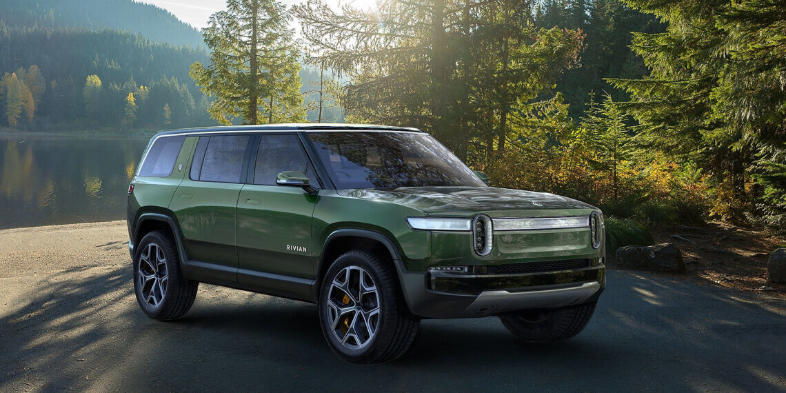 Green Rivian R1S electric SUV parked in a natural setting with trees and sunlight.