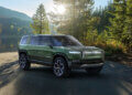 Green Rivian R1S electric SUV parked in a natural setting with trees and sunlight.