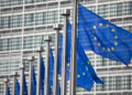 Row of European Union flags waving in front of a modern glass building.