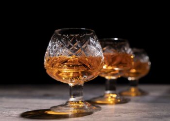 Three crystal glasses filled with amber cognac on a dark background.