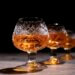 Three crystal glasses filled with amber cognac on a dark background.