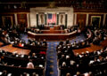 A view of the U.S. Congress chamber with members seated and the American flag displayed.