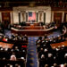 A view of the U.S. Congress chamber with members seated and the American flag displayed.