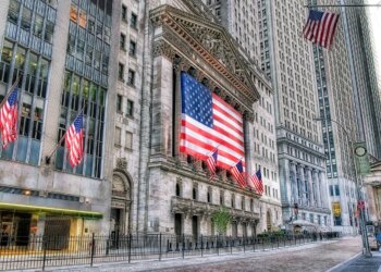 Facade of the New York Stock Exchange featuring a large American flag and multiple smaller flags.
