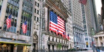 Facade of the New York Stock Exchange featuring a large American flag and multiple smaller flags.