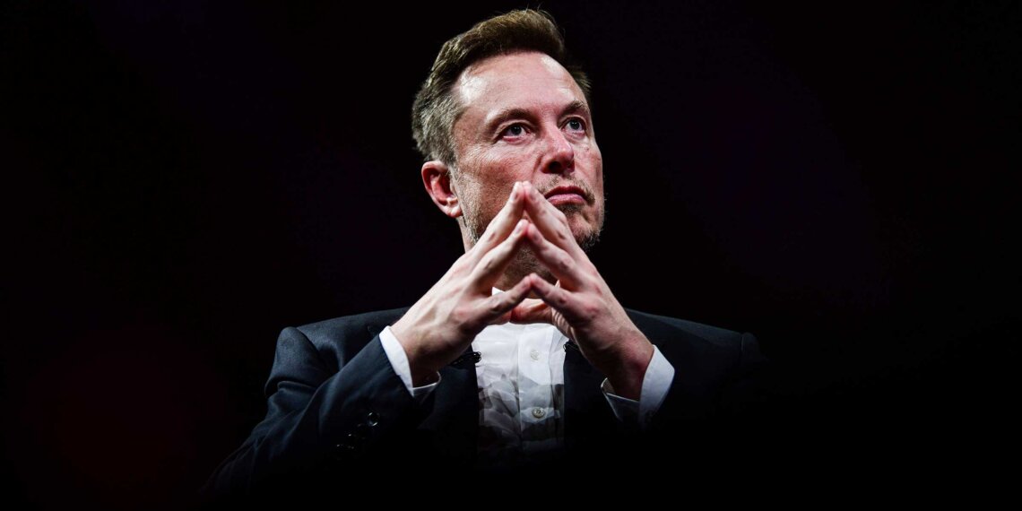 Elon Musk seated with hands clasped, wearing a suit and looking thoughtfully ahead against a dark background.