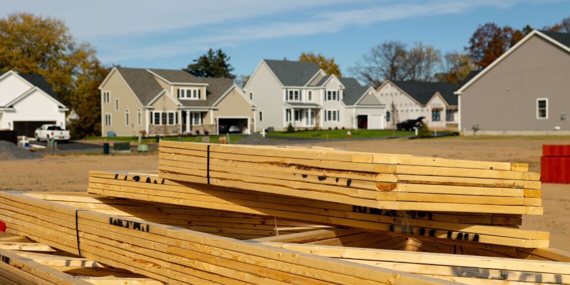 Stack of wooden lumber in front of residential houses under construction.