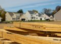 Stack of wooden lumber in front of residential houses under construction.