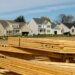 Stack of wooden lumber in front of residential houses under construction.