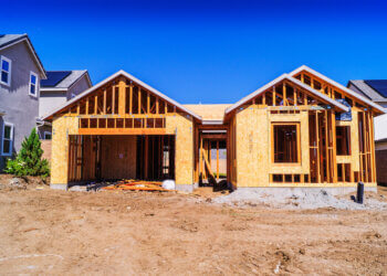 A residential building under construction with wooden framing and a clear blue sky.
