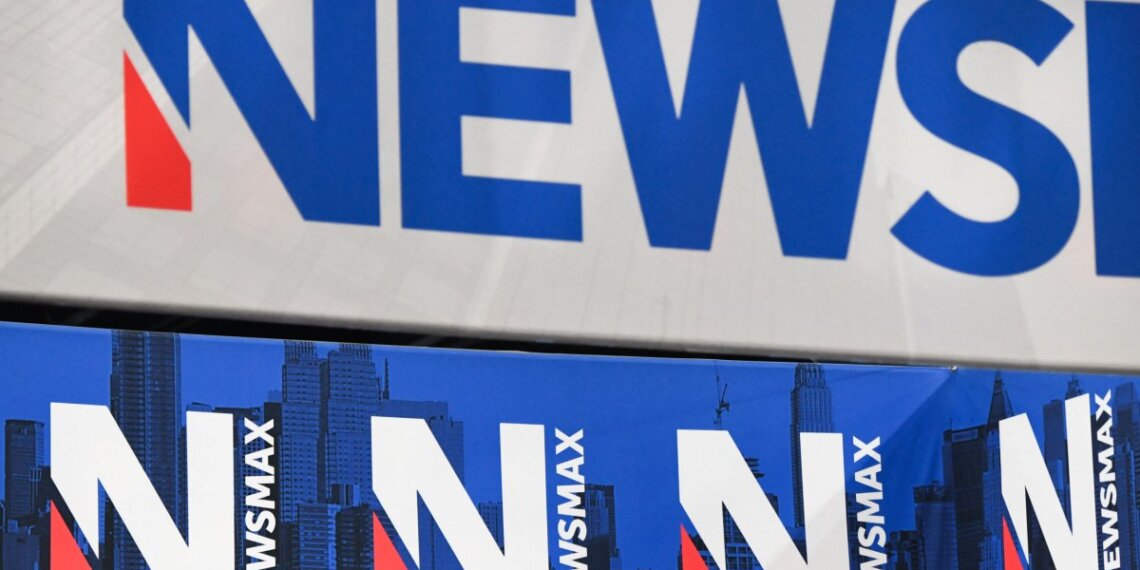 Signage displaying the Newsmax logo in blue and red colors against a white background.