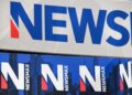 Signage displaying the Newsmax logo in blue and red colors against a white background.