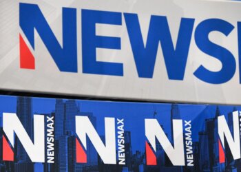 Signage displaying the Newsmax logo in blue and red colors against a white background.