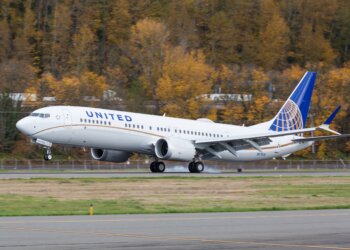 United Airlines Boeing 737 airplane taking off on a runway with autumn trees in the background.