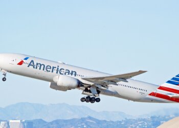 American Airlines Boeing 777 aircraft taking off with a clear sky in the background.