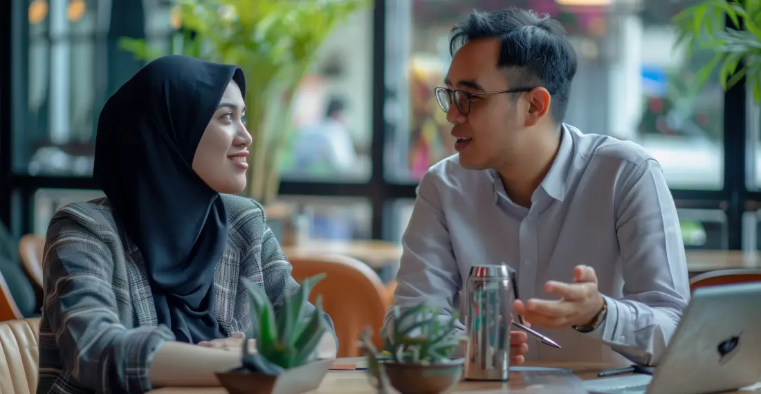 A man and a woman sitting at a table, engaged in conversation in a cafe setting.