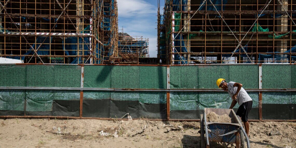 Construction worker pushing a wheelbarrow filled with sand at a construction site with scaffolding.