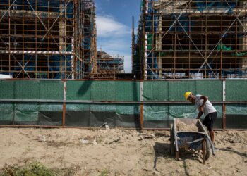 Construction worker pushing a wheelbarrow filled with sand at a construction site with scaffolding.