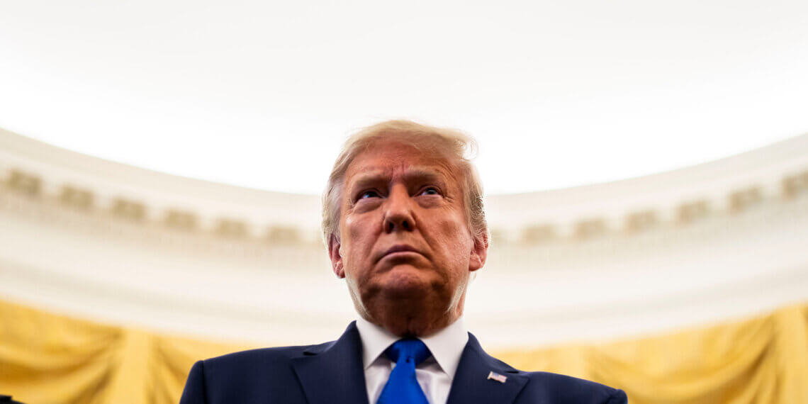 Donald Trump wearing a dark suit and blue tie, looking serious in a formal setting.