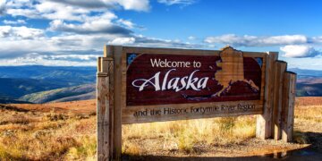 Wooden sign that reads 'Welcome to Alaska' with a map of Alaska and scenic background.