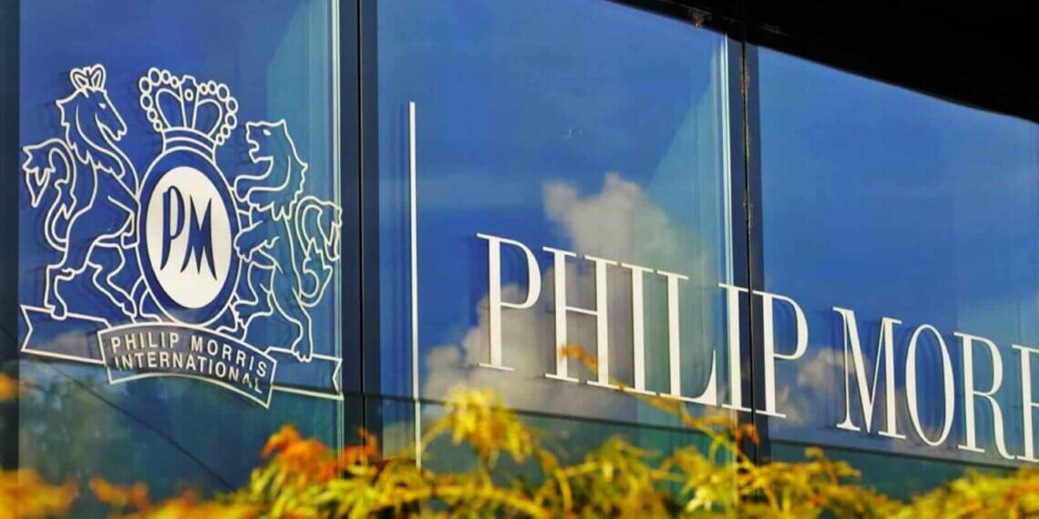 Philip Morris International logo displayed on a glass building with decorative foliage in the foreground.