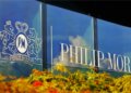 Philip Morris International logo displayed on a glass building with decorative foliage in the foreground.